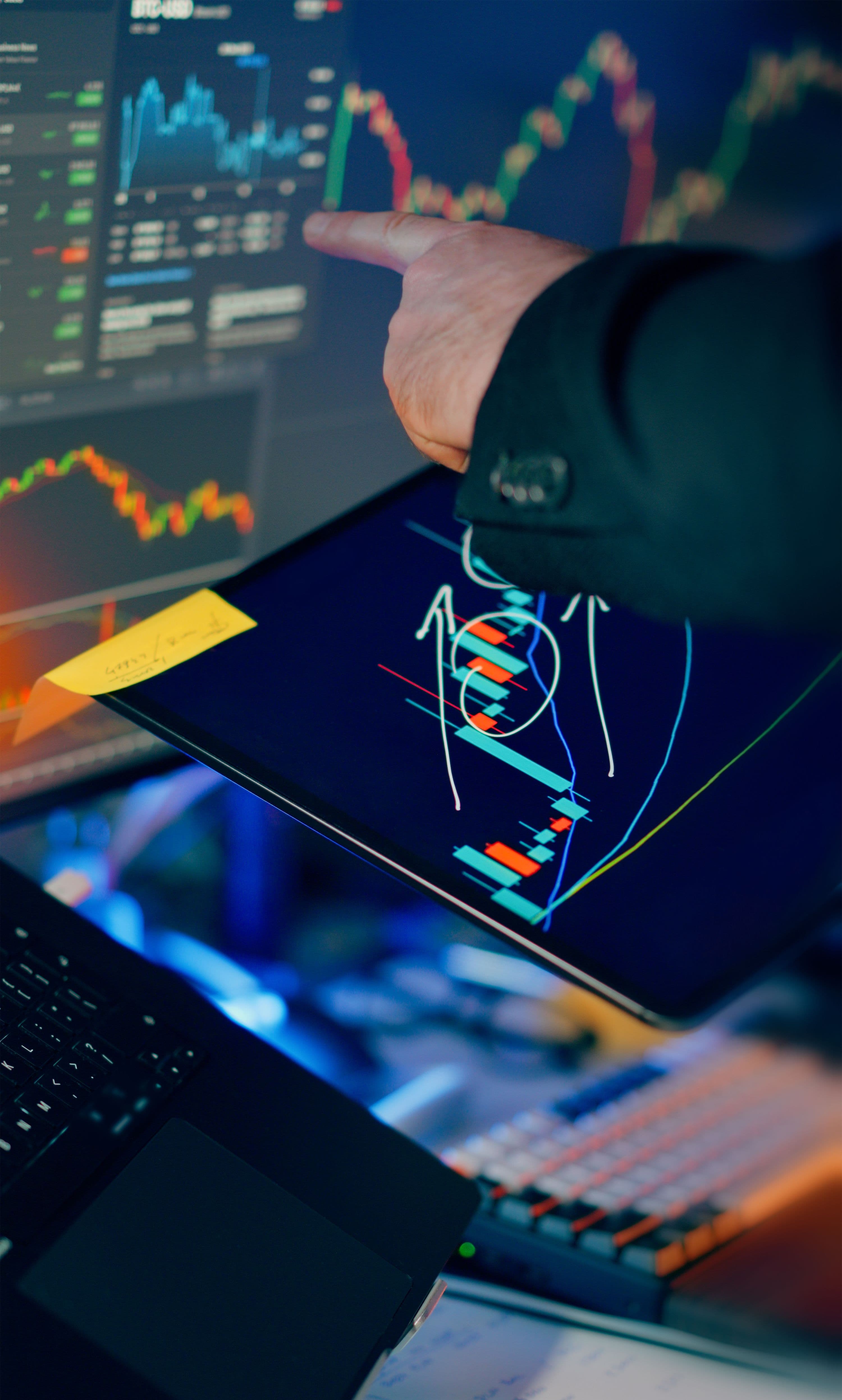 A professional examining candlestick charts and market data across a tablet and laptop screen